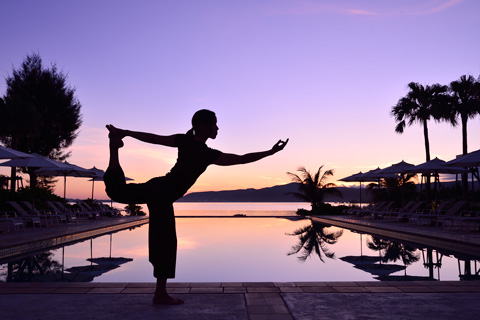 a lady holding a yoga pose in front of the swimming pool